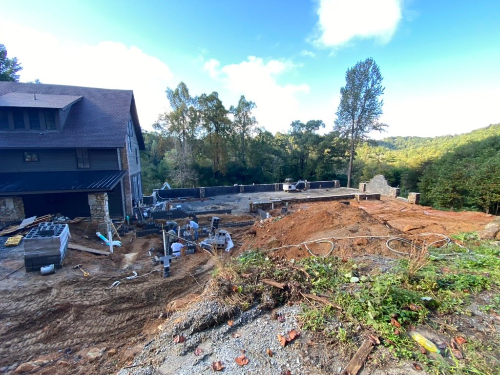 Wide view — inn and terrace walls mid-construction with Blue Ridge treeline beyond