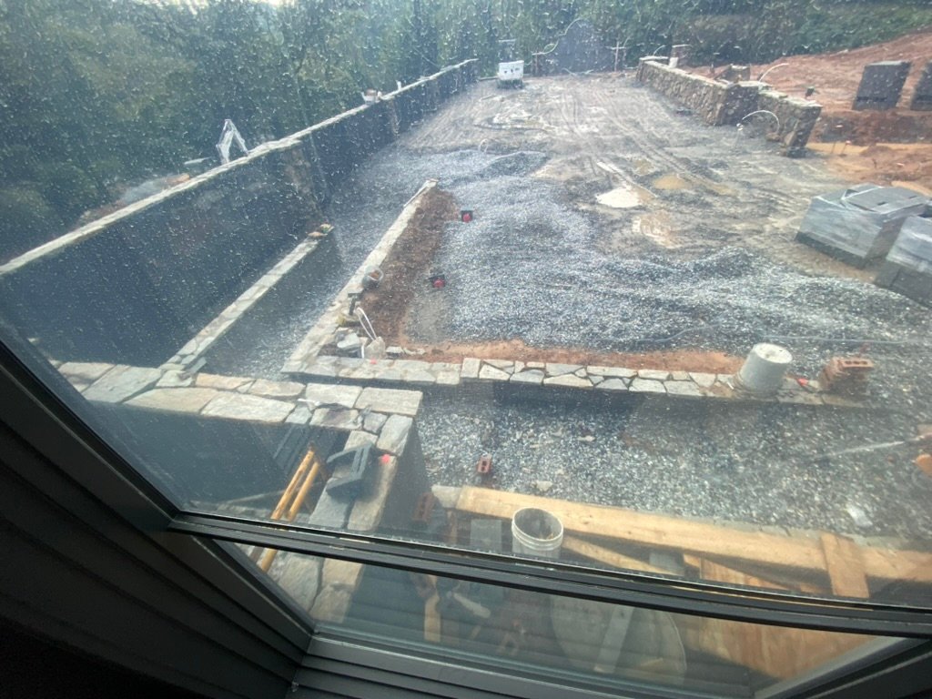 Terrace gravel base — bluestone layout beginning, viewed through rain-streaked window