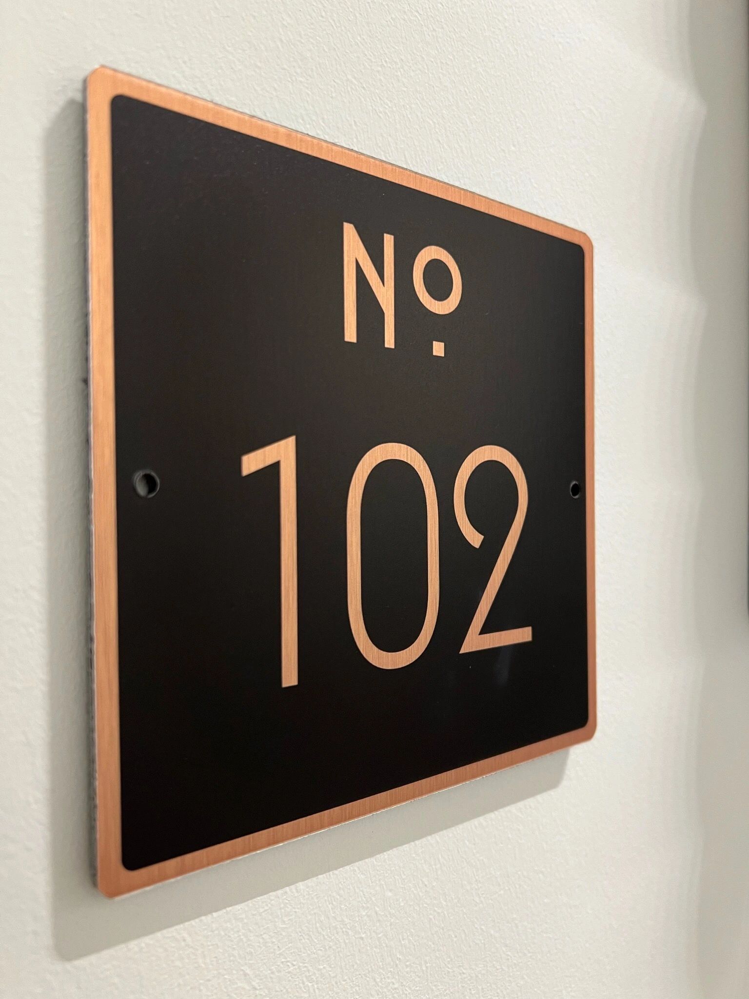 Black and copper room number sign reading No. 102 on a white wall
